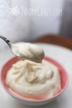 a spoon full of cream sitting on top of a white plate with a pink bowl