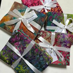 four small gift boxes with ribbons tied around them on a white counter top, each containing different designs and colors