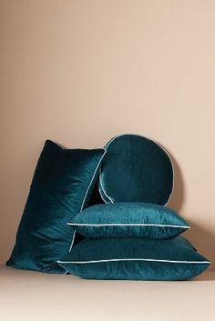 three blue pillows stacked on top of each other in front of a beige wall with white piping