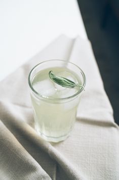 a glass filled with water sitting on top of a white cloth covered table next to a bottle