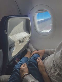 a man and woman sitting on an airplane seat with their feet up looking out the window