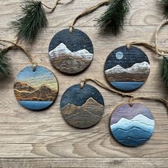 four handmade ceramic ornaments hanging from twine on a wooden table with pine branches