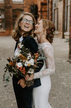 two brides are hugging each other in front of an old building with brick walls