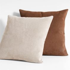 two pillows sitting next to each other on top of a white surface with one brown pillow