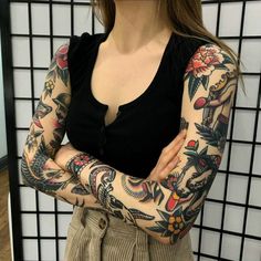 a woman with tattoos on her arms standing in front of a wall