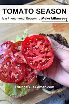 a person holding a tomato on top of a hamburger