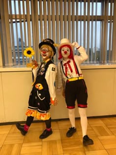 two clowns dressed in costumes standing next to each other with sunflowers on their heads