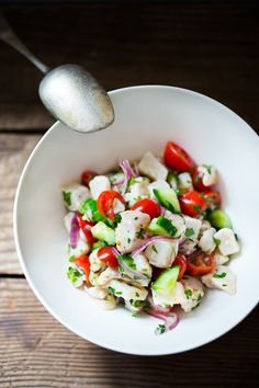 a white bowl filled with salad on top of a wooden table next to a spoon