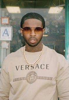 a man wearing sunglasses standing in front of a store window with his hand on his hip