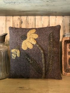 a brown pillow with yellow flowers on it sitting on a table next to a vase