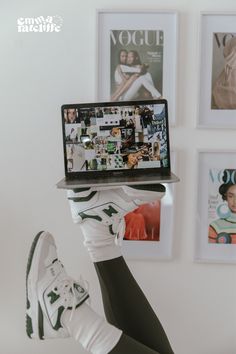 a person holding up a laptop computer in front of their face with pictures on the wall behind them