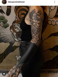 a woman with a tattoo on her arm and hand is standing in front of a wall