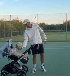 a man standing on a tennis court with a baby in a stroller