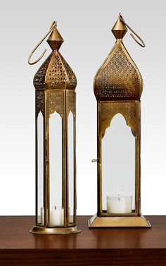 two brass lanterns with candles on a wooden table next to each other and one has a candle in it