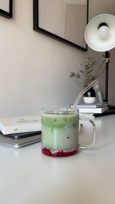 a glass mug with liquid inside sitting on a table next to a book and lamp