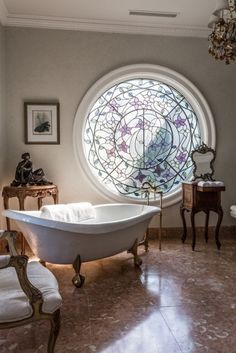 a bath tub sitting next to a window in a bathroom under a circular stained glass window