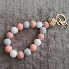 a pink, white and grey beaded bracelet with a gold keychain on a gray blanket