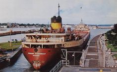 two large ships are docked in the water at a dock with people standing on either side