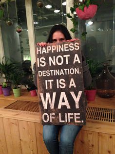 a woman holding a sign that says happiness is not a destination it is a way of life