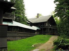 an old log house in the woods with green grass and trees on either side of it