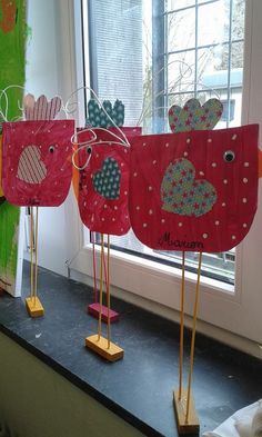 three red and green paper birds sitting on top of a counter next to a window