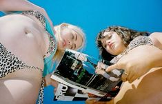 two women in bikinis are posing for the camera with one holding a photo album