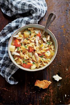 a bowl of chicken noodle soup on a wooden table with a black and white checkered napkin