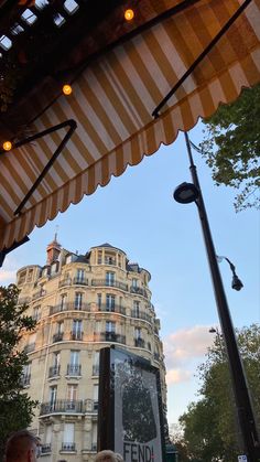 people are sitting under an awning in front of a tall building with many windows