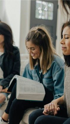 three women sitting on a couch looking at an open book