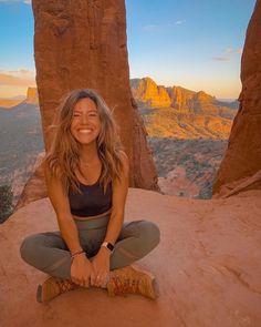 a woman sitting on top of a rock with mountains in the background