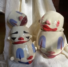 two ceramic clowns sitting next to each other on a white cloth covered tablecloth