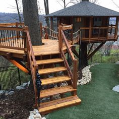 a tree house with stairs leading up to the top and bottom floor, surrounded by grass