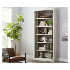 a white bookcase with books on it in a living room next to a chair and potted plant