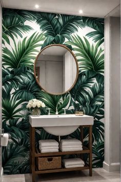 a bathroom with palm leaves on the wall and a round mirror above it, along with white towels