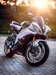 a black and silver motorcycle parked on top of a brick road in front of the sun