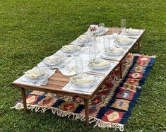 a table set with plates and silverware on a rug in the middle of a field