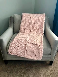 a gray chair with a pink blanket on it in front of a blue wall and carpet