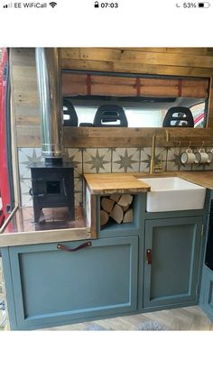 a kitchen with blue cabinets and wood burning stove in the back wall, next to a sink