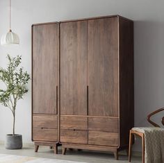 a wooden armoire next to a chair and potted plant