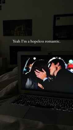 an open laptop computer sitting on top of a bed next to a couple kissing each other