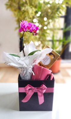 a small black box with pink flowers and chocolates in it on a table next to a potted plant