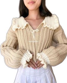 a woman wearing a sweater with ruffles on the shoulders and long sleeves, standing in front of a white background