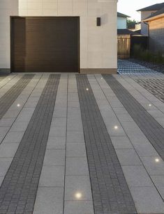 an empty driveway with two garage doors in the background and lights on either side of it