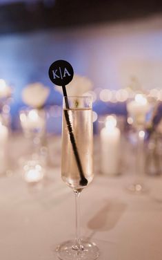 a wine glass with a black stick sticking out of it sitting on a table in front of candles