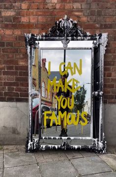 a mirror sitting on the side of a street next to a brick wall with graffiti written on it