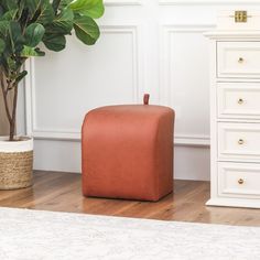 an orange ottoman sitting on top of a wooden floor next to a potted plant