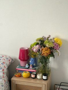 a table with flowers and books on it next to a bed in a room that has white walls