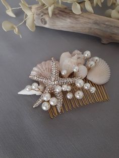 a starfish comb with pearls and seashells sits on a table next to a branch