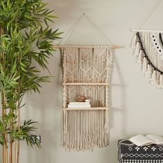 a room with a plant and some books on the shelf next to a wall hanging