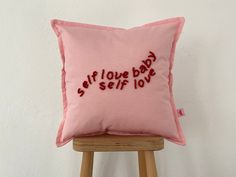 a pink pillow with the words self love baby on it sitting on a wooden stool